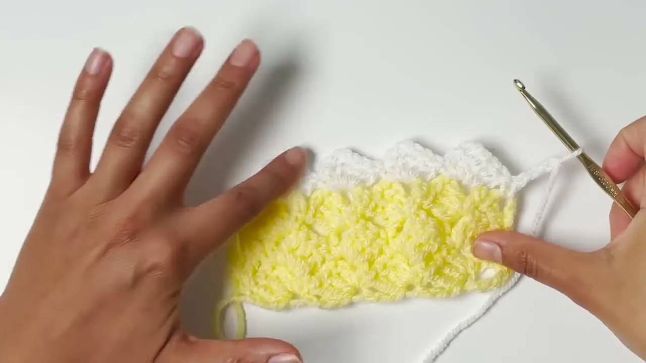 Finished crochet sample in sunny yellow with a white scalloped border, held in hands